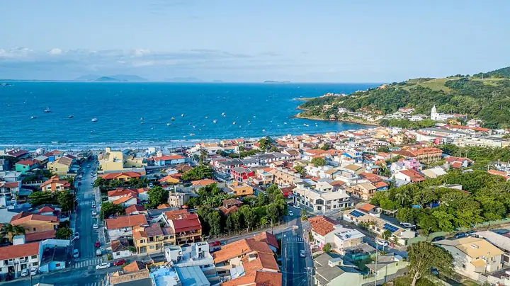 Vista aérea de cidade litorânea com casario de telhados vermelhos, a enseada e o mar ao fundo