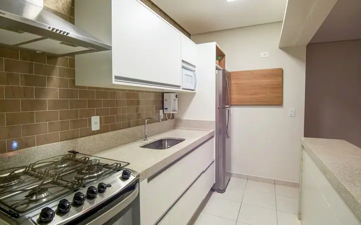 Cozinha planejada com fogão de cinco bocas, coifa de inox, armários brancos e revestimento cinza