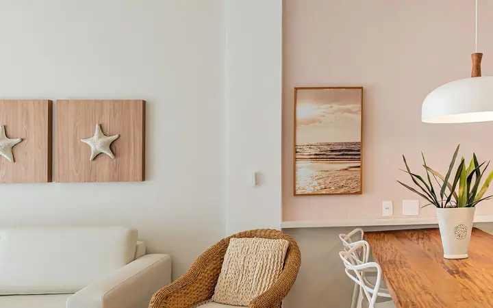 Living de apartamento com quadros de estrela-do-mar em madeira, poltrona de fibra natural e mesa de madeira