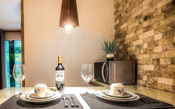 Detalhe de mesa posta com garrafa de vinho, taças e louça diante de parede de pedra