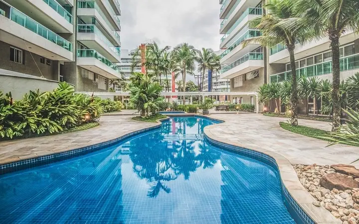 Piscina de condomínio residencial entre prédios de varandas de vidro, coqueiros e jardim